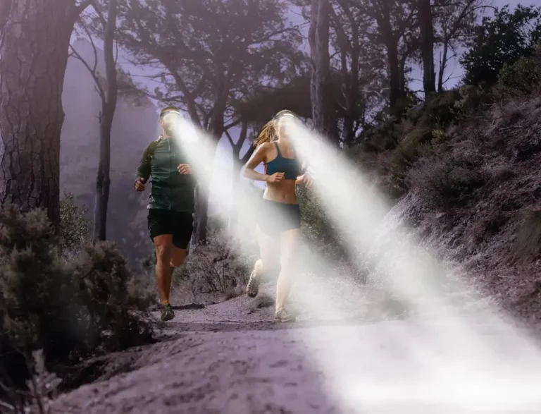 Due jogger con le lampade frontali che corrono nella foresta