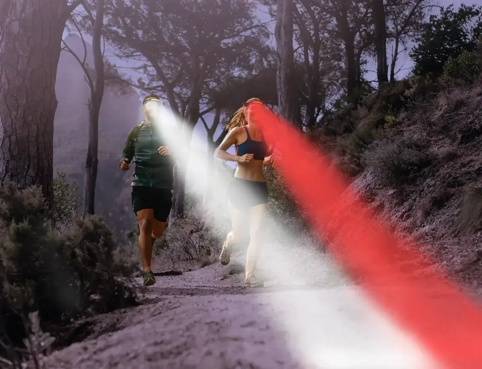 Two joggers wearing headlamps, running through the forest