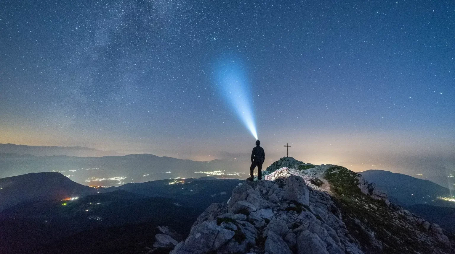 A person with a headlamp at the top of a mountain at night