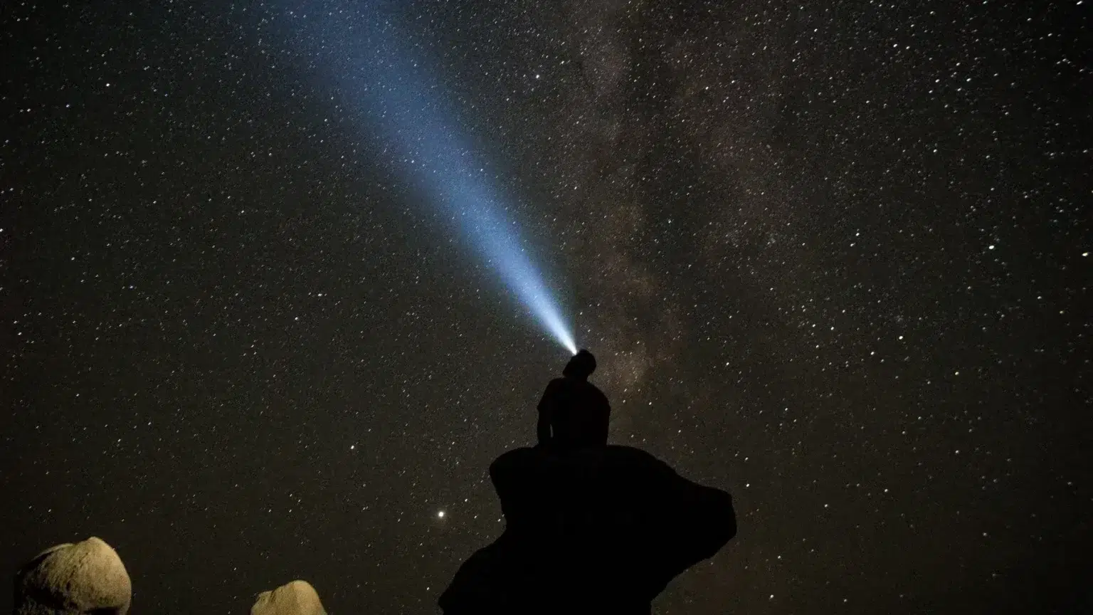 Una persona seduta su una roccia di notte che guarda le stelle