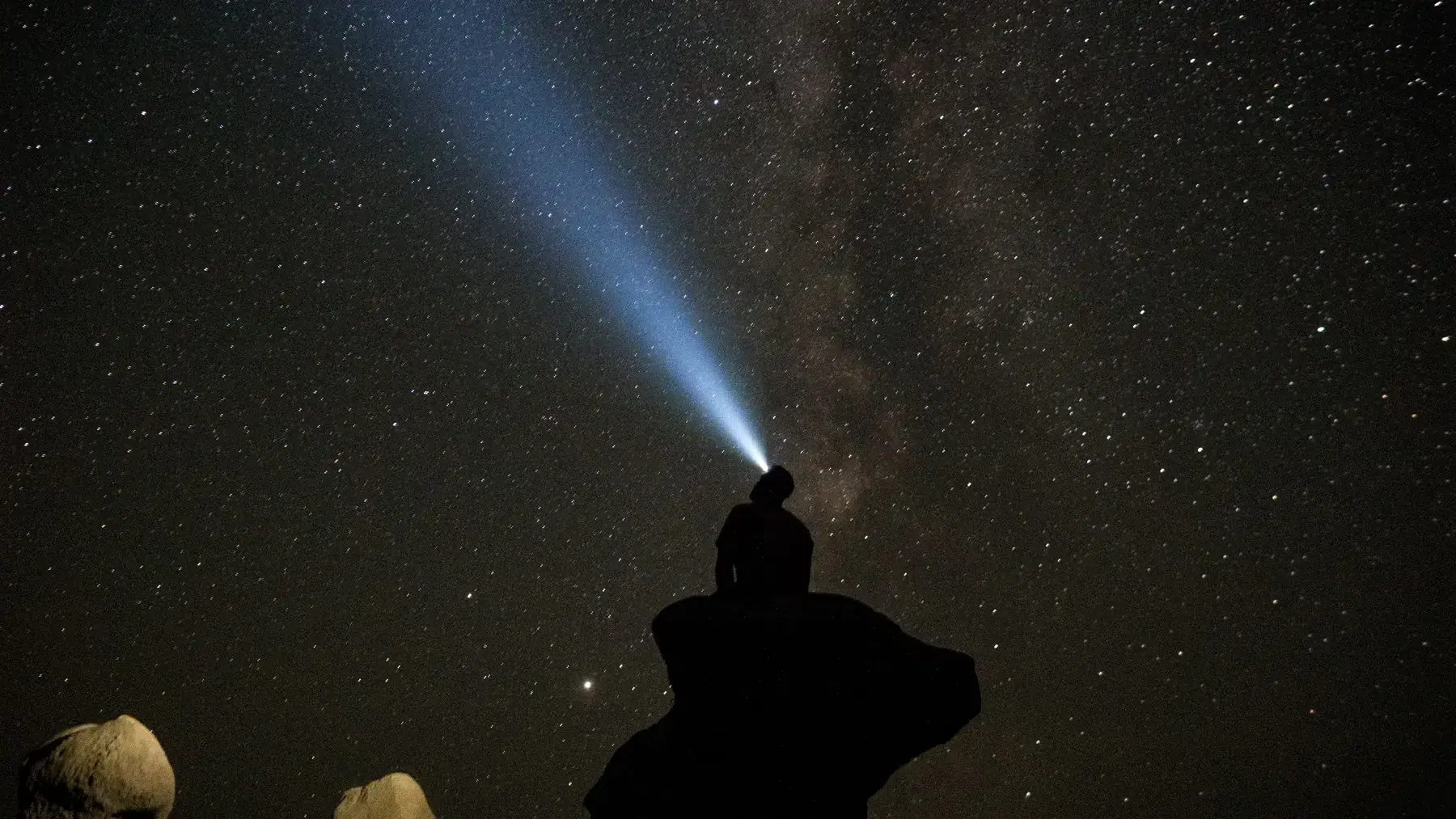 Une personne assise sur un rocher la nuit regardant les étoiles